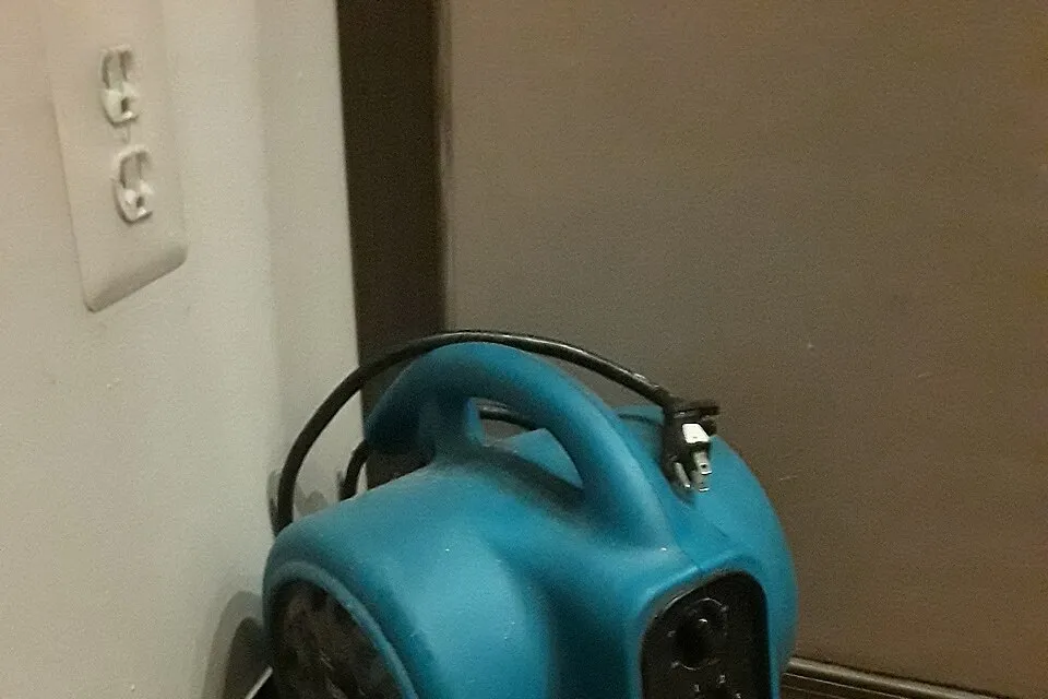Portable air mover beside an interior wall, representative drying equipment